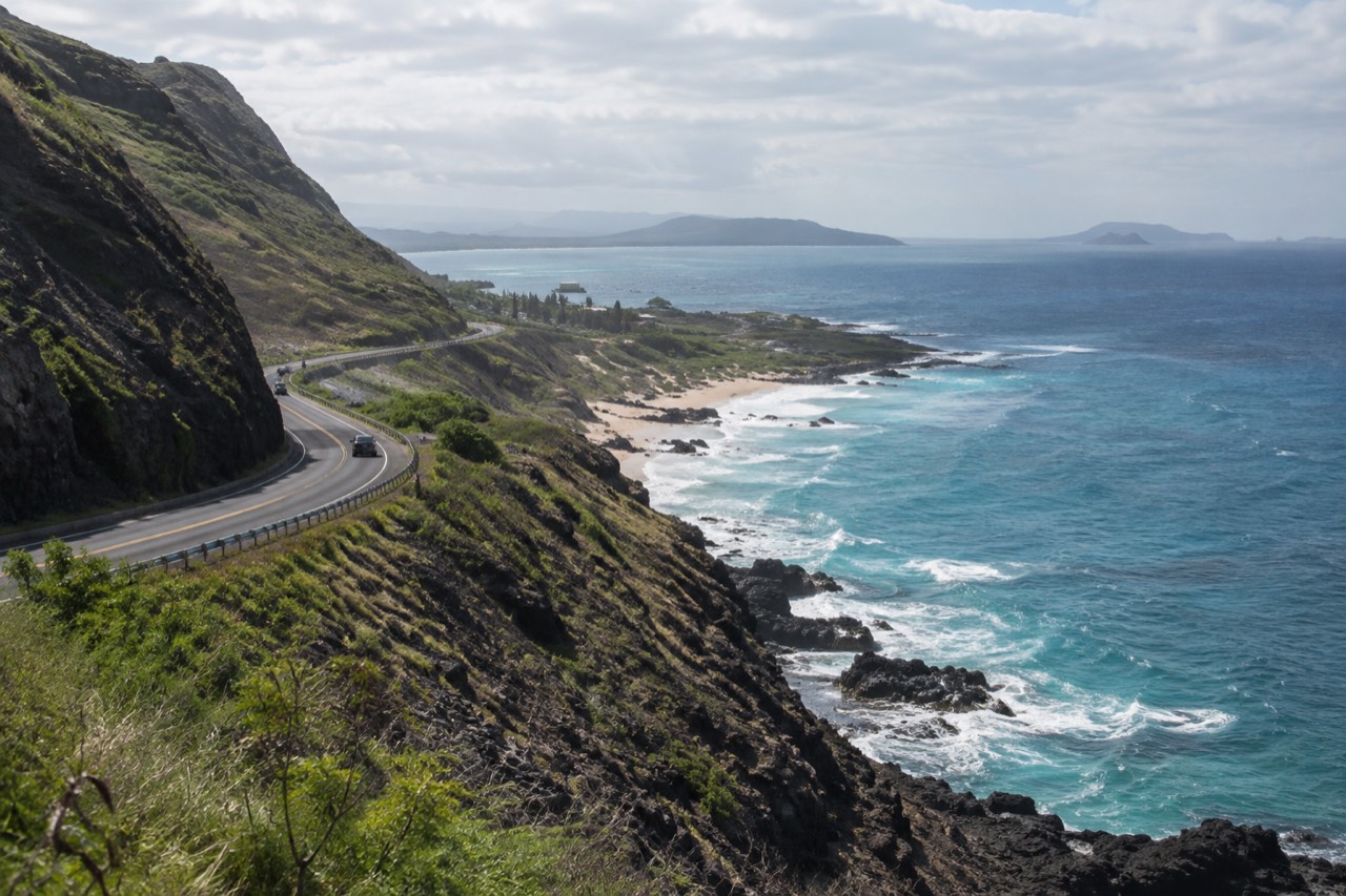 A coastal highway on Oahu winding past green cliffs with blue ocean beyond