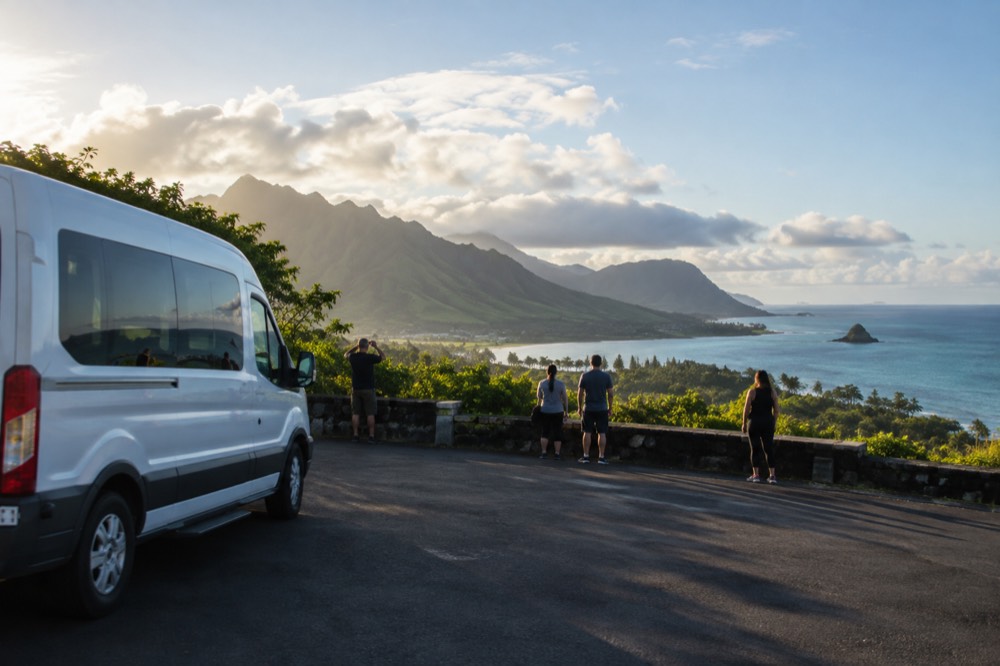 A tour van parked at a windward coast lookout with green ridges and turquoise water below