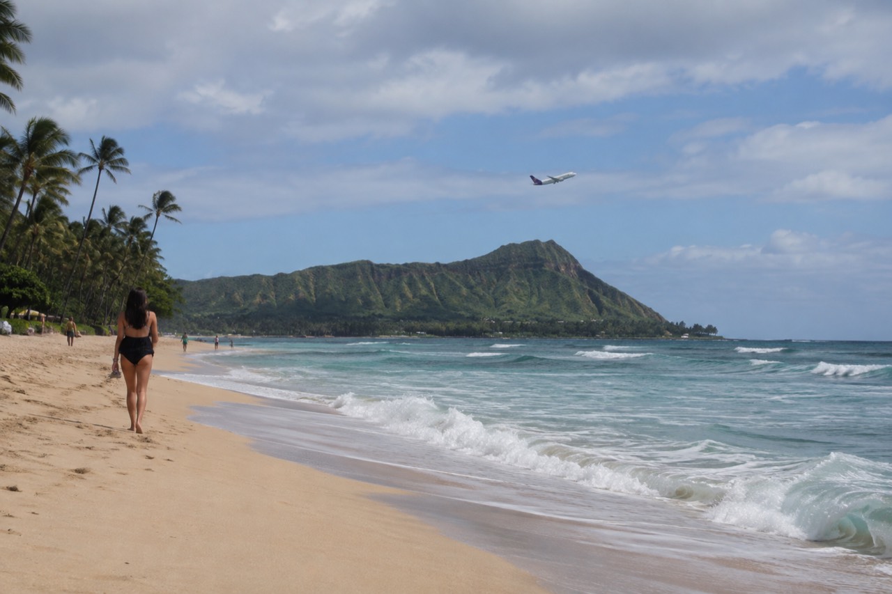 A small interisland jet climbing over a green Oahu ridge toward open blue sky