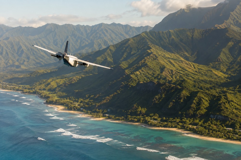 A small interisland passenger aircraft banking over green Kauai ridges above a turquoise coastline