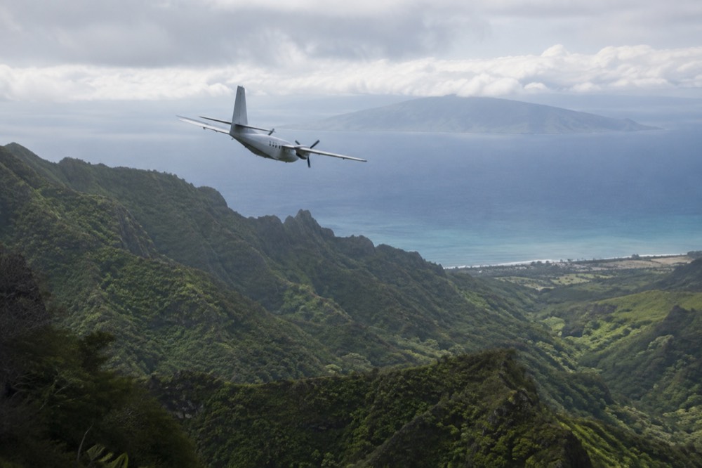 A small interisland passenger aircraft banking over green Maui valleys with the ocean beyond