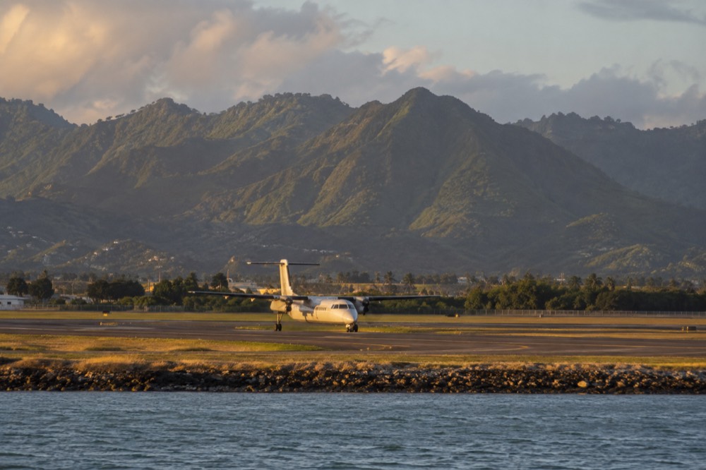 A commuter aircraft on a runway in Hawaii with green mountains behind it