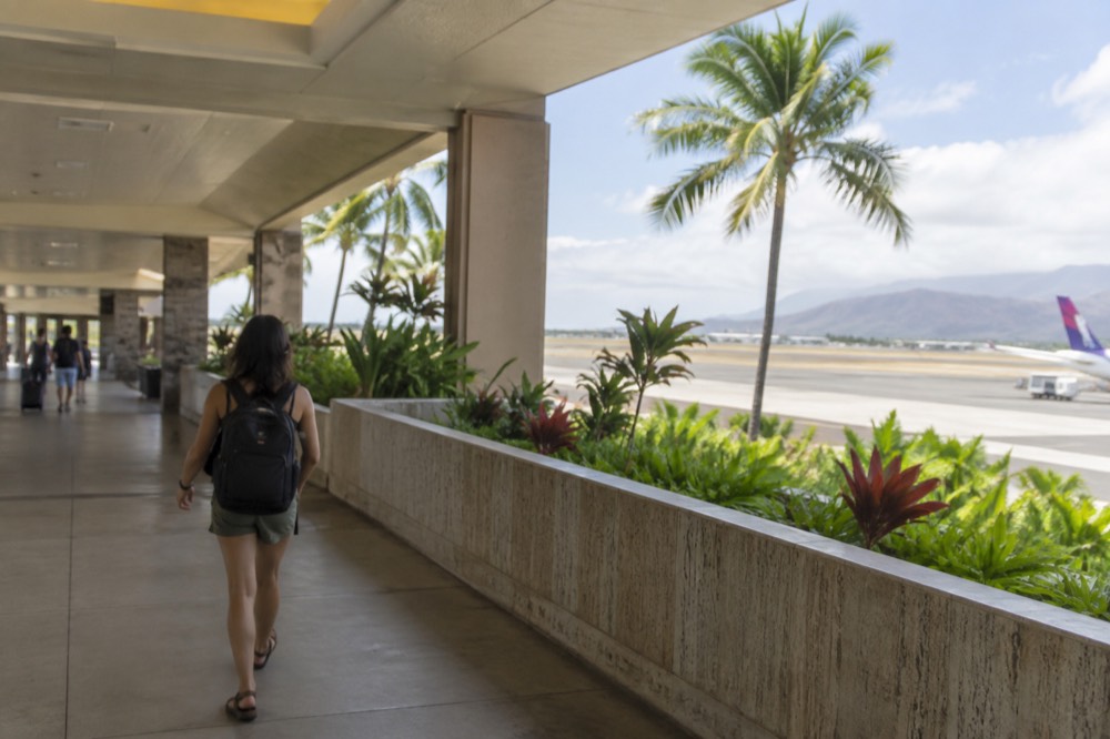 A traveller with a small backpack walking through a bright open-air airport corridor in Hawaii