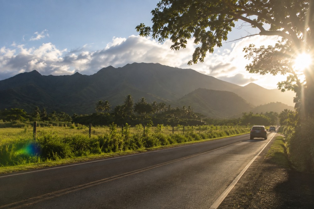 A two-lane highway running beside green fields and mountains on the windward side of Oahu