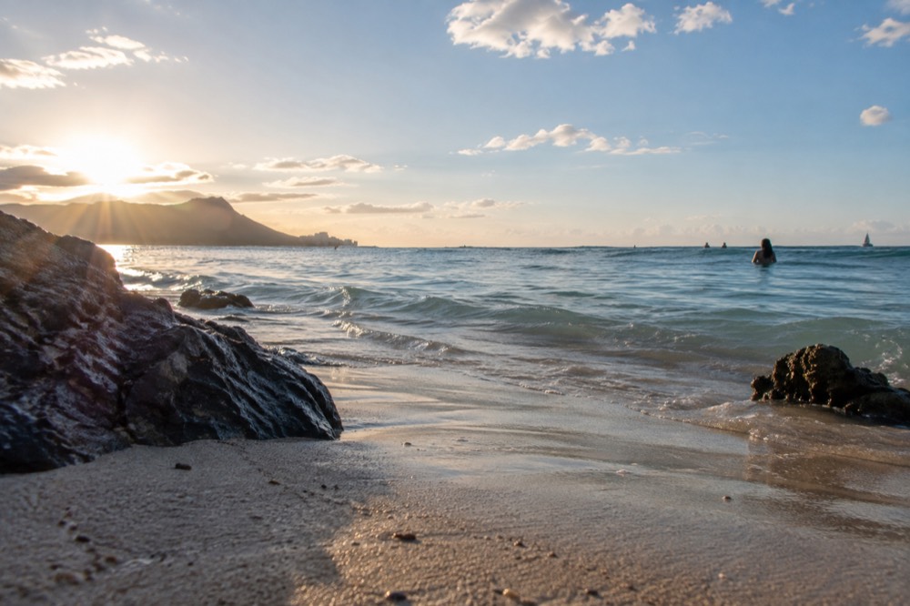Calm turquoise water over a sandy Oahu beach with a swimmer wading near shore