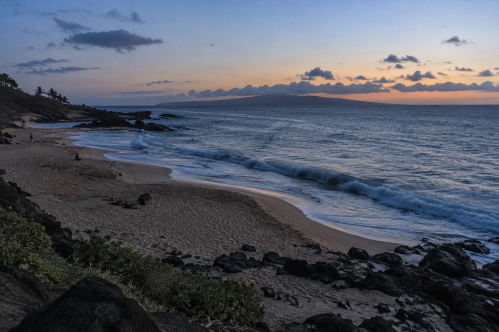 A wide sandy beach with rocky points at each end and small waves breaking offshore