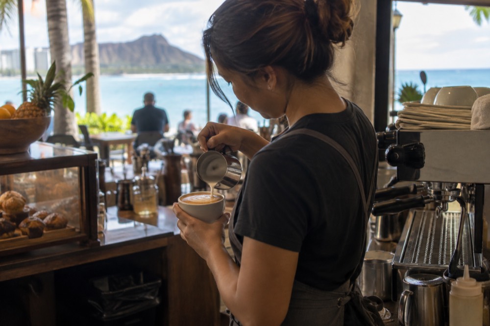 A barista pouring steamed milk into a latte at a small café counter