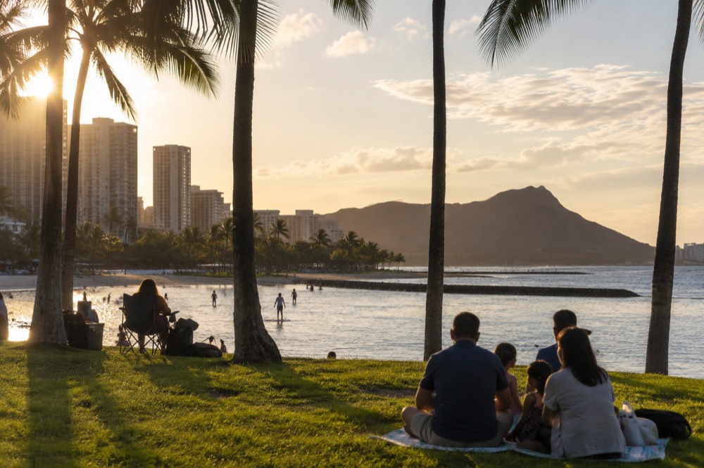 Families relaxing on a grassy lawn beside a resort lagoon in the late afternoon