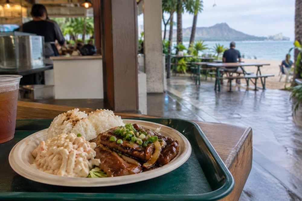 A plate lunch with rice, macaroni salad and a main dish served on a cafeteria tray at a casual Oahu counter