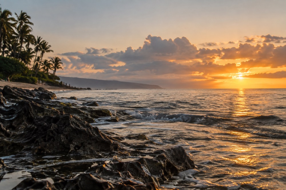 Golden light over the ocean along Oahu's western shore with distant clouds catching the last sun