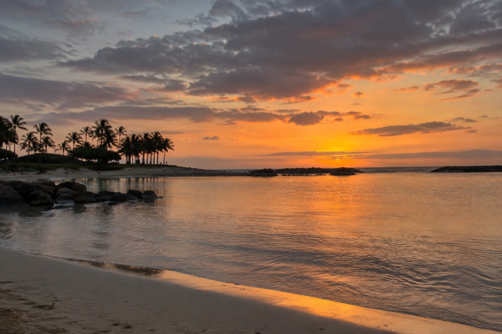 A calm lagoon at Ko Olina at dusk with still water reflecting orange sky