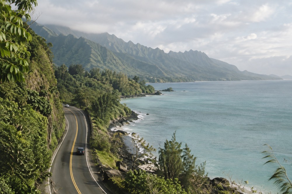 A two-lane highway curving along the green windward coast of Oahu with the ocean on one side