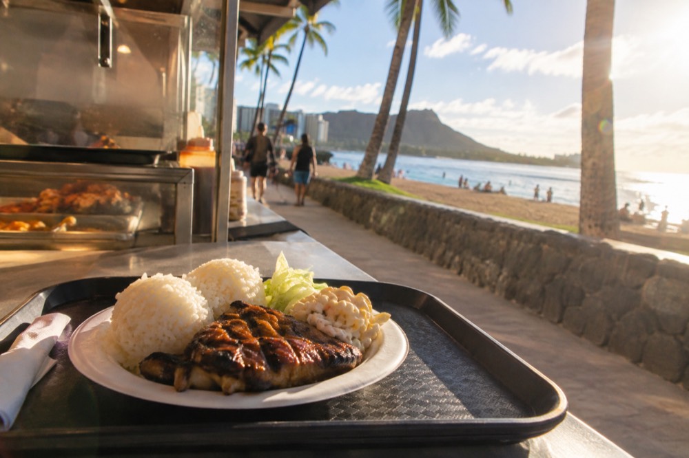 A plate lunch with rice and grilled protein served on a cafeteria tray at an Oahu food counter