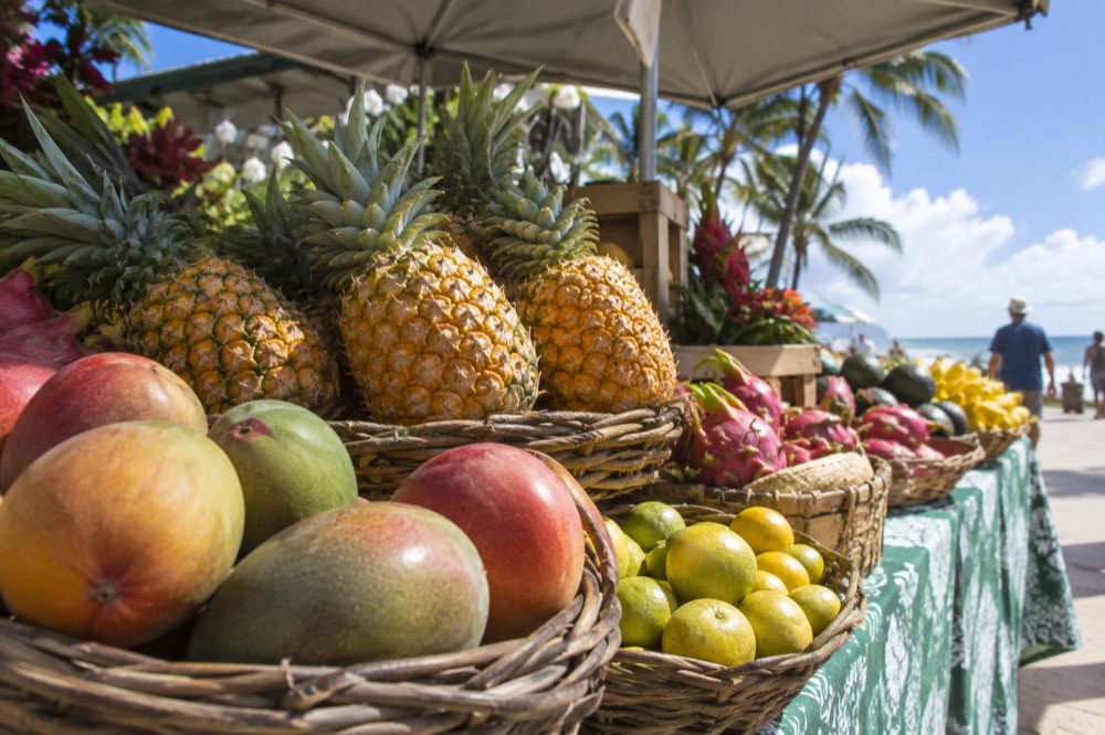 A shaded farmers market stall on Oahu with tropical fruit arranged in baskets under a canopy
