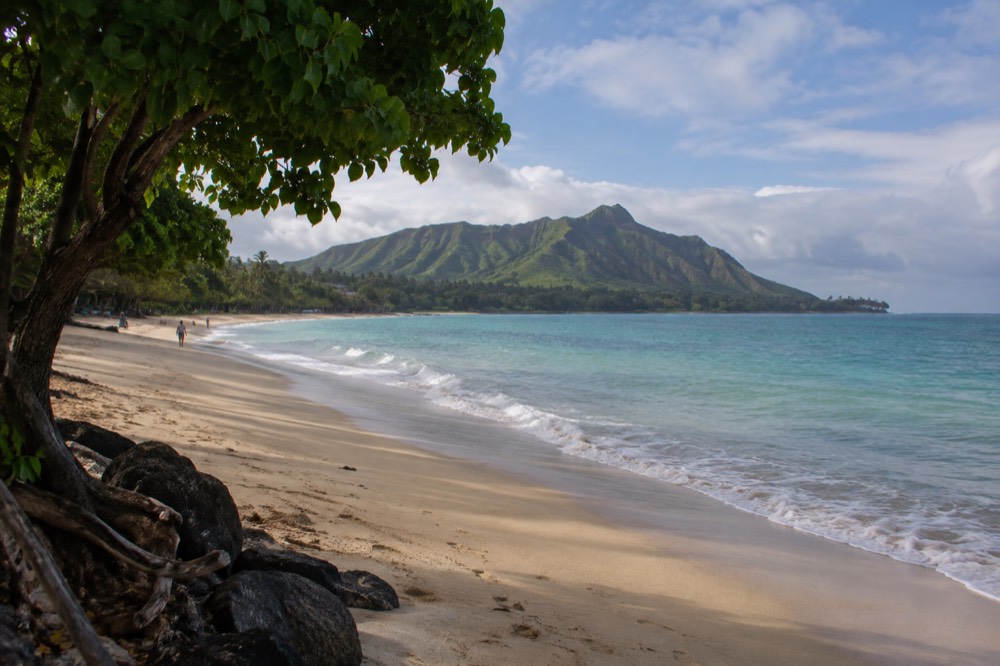 A calm windward beach on Oʻahu with green ridges and a mostly empty stretch of sand