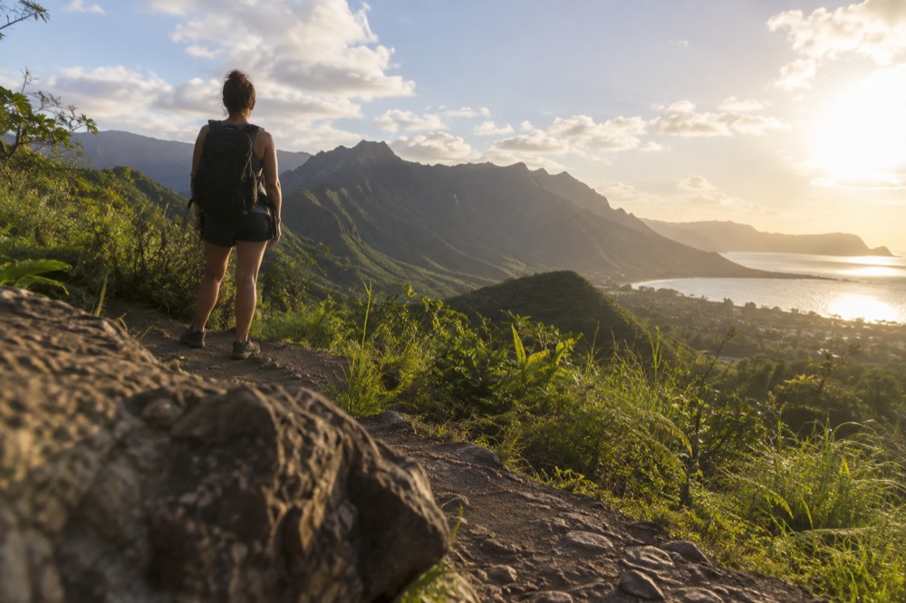 A hiker on a ridge trail looking toward Oahu's green Koʻolau mountains