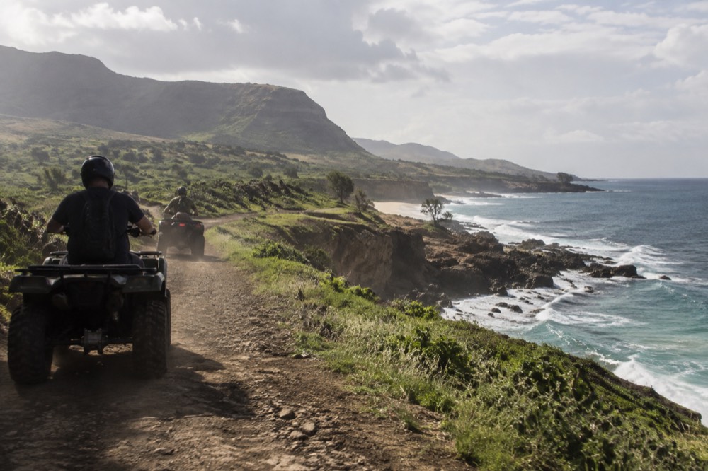 A rider on an all-terrain vehicle following a guide along a coastal dirt trail on Oahu