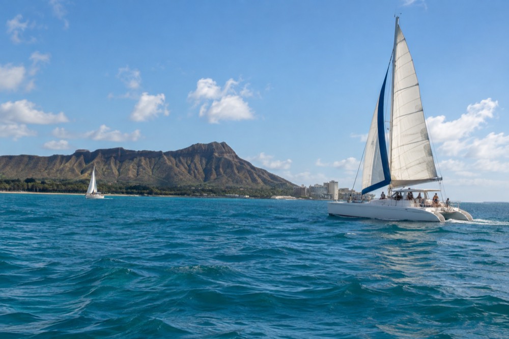 A catamaran under sail off the Waikiki coastline with Diamond Head in the distance