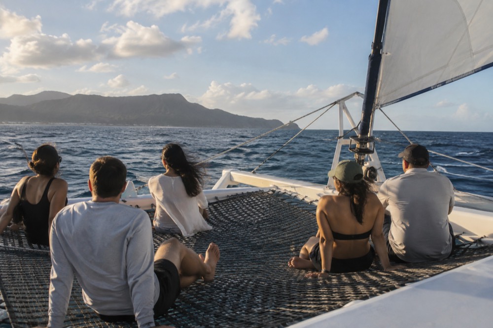 Passengers seated on the trampoline netting at the front of a catamaran as the boat heels in open water