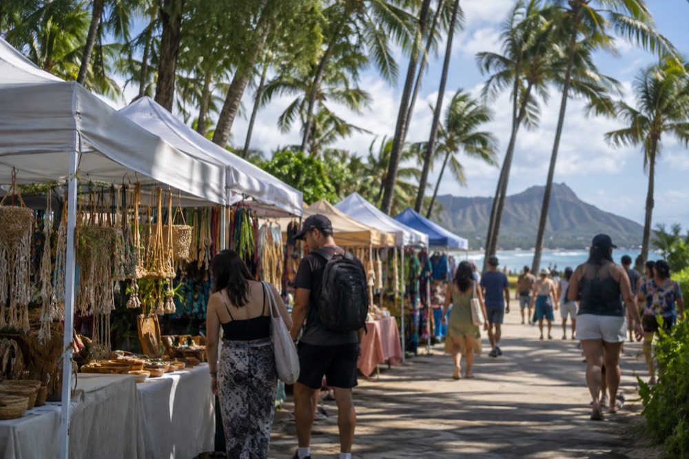 Visitors browsing stalls at an open-air market under palm trees on Oahu