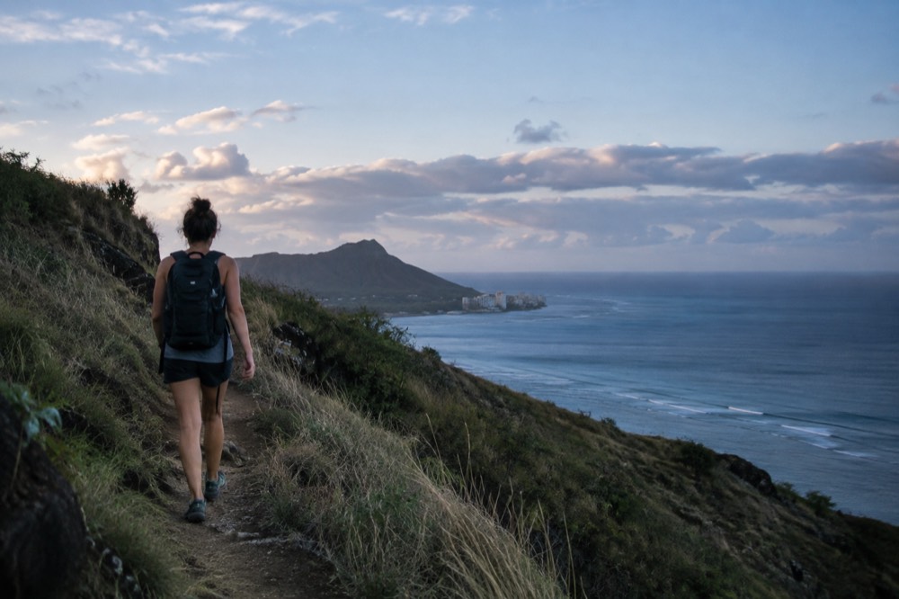 A hiker walking a ridgeline trail above the Honolulu coastline in morning light