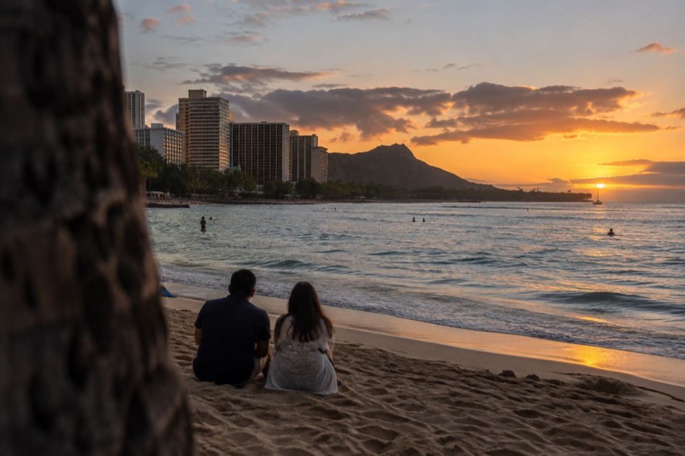 A couple watching the sun set over the ocean from a Waikiki beach with the skyline behind them