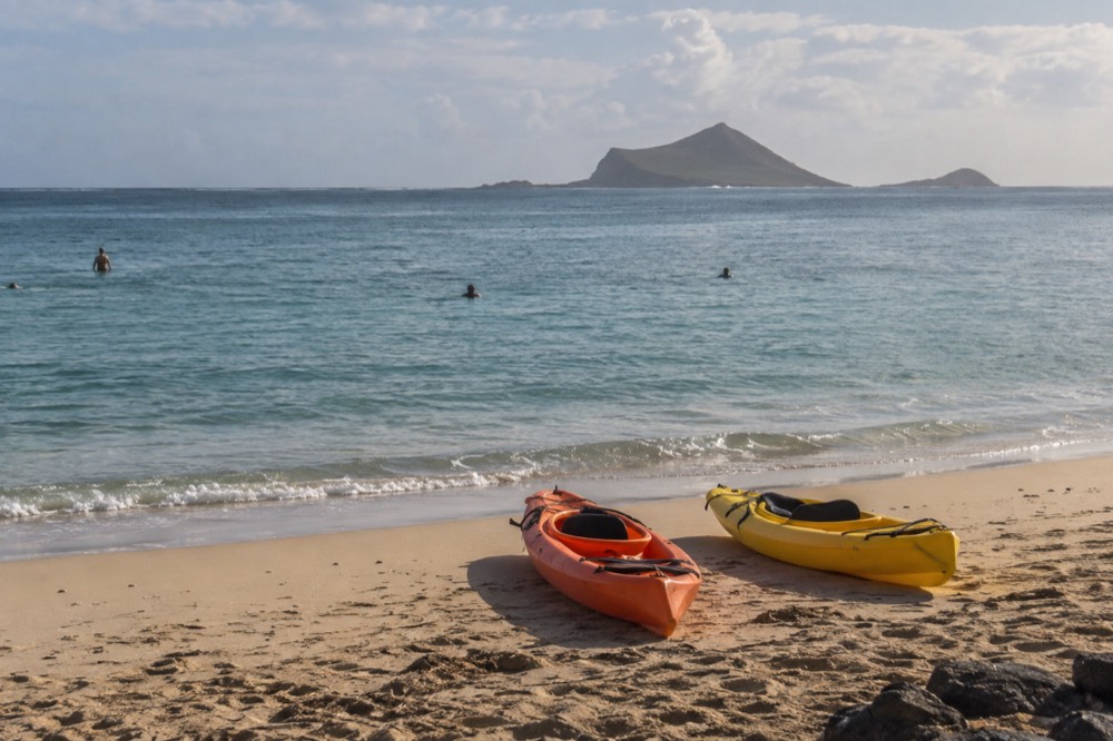 Two kayaks resting on a calm windward beach with small offshore islands in the distance