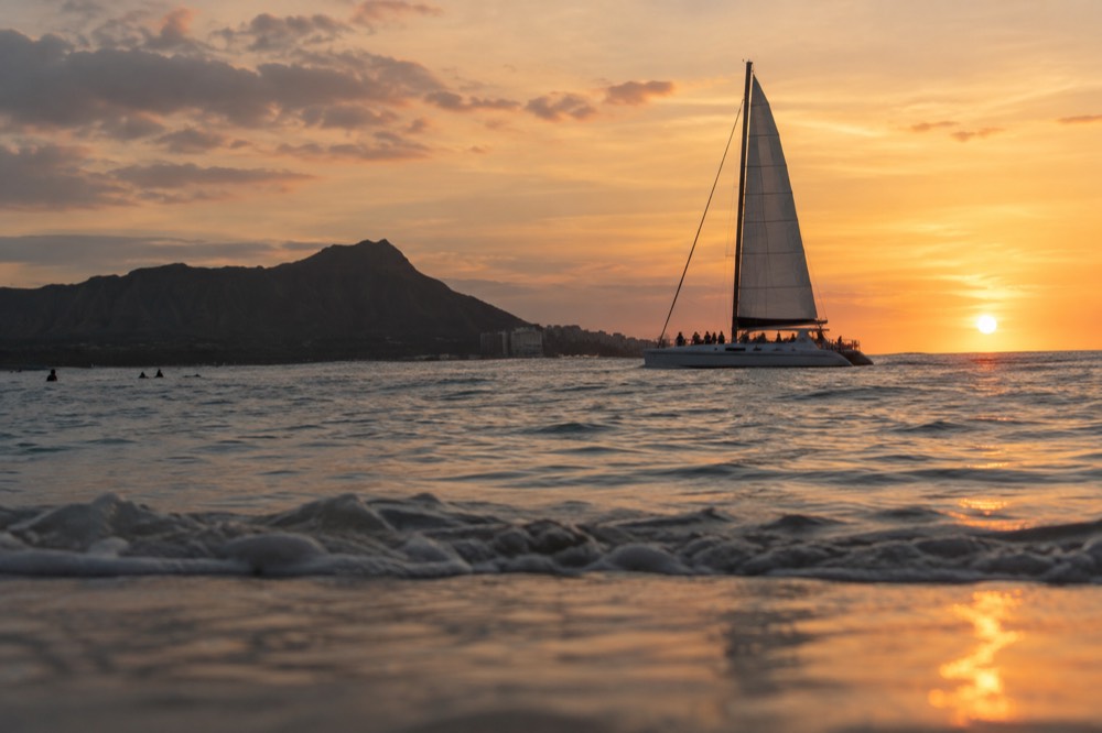A catamaran under sail off Waikiki in the last orange light before sunset
