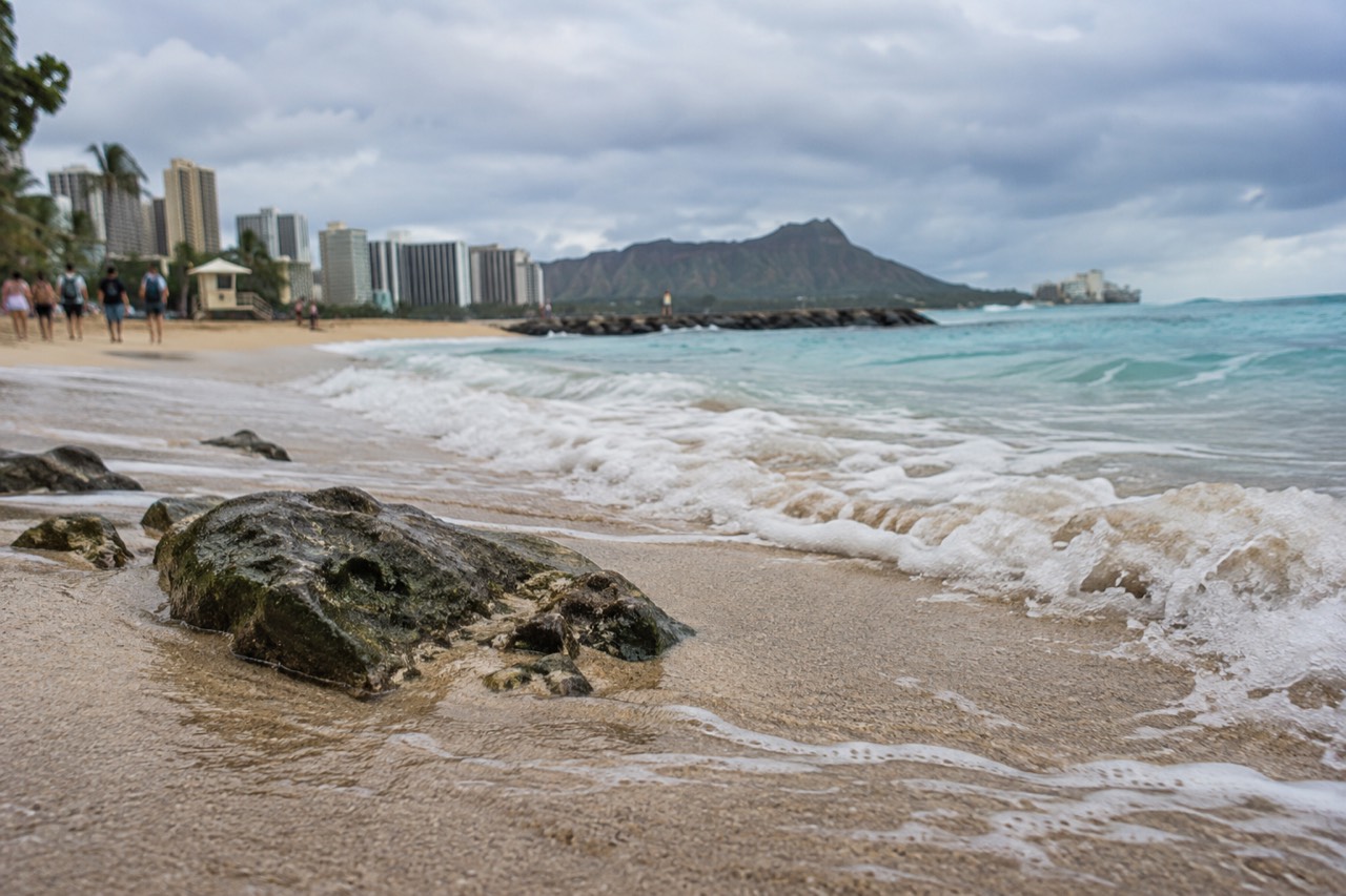 Turquoise ocean rolling onto a wide Oahu beach with a lifeguard tower in the distance