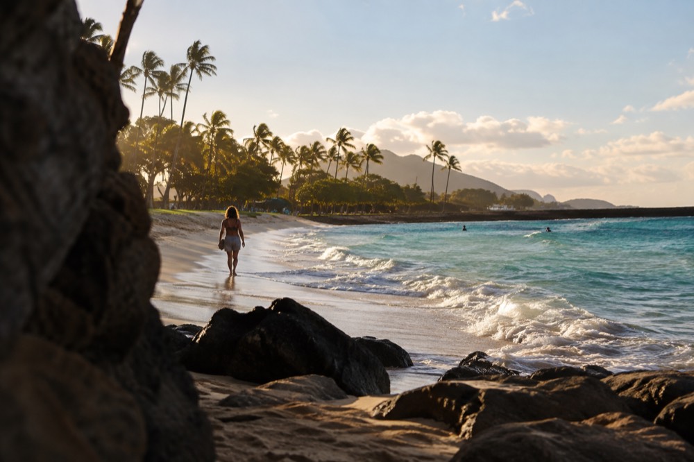 A wide sandy beach on Oahu with turquoise water and palm trees along the shore