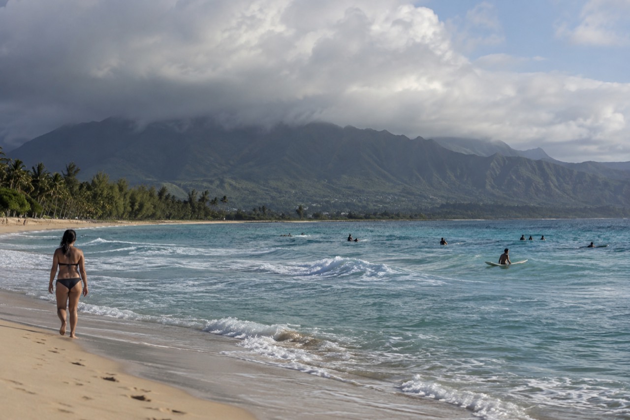 Rain clouds passing over the green Koʻolau mountains above a sunny Waikīkī beach