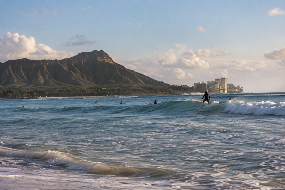 Surfer riding a gentle wave off a Waikiki beach with Diamond Head in the distance