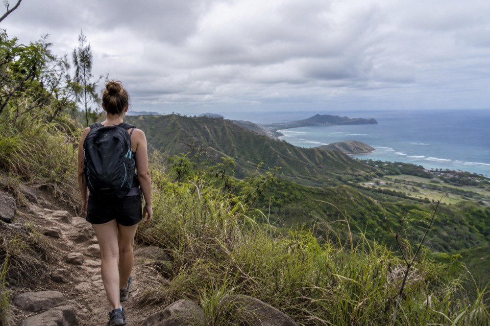 A hiker on a ridge trail overlooking a green valley and the ocean