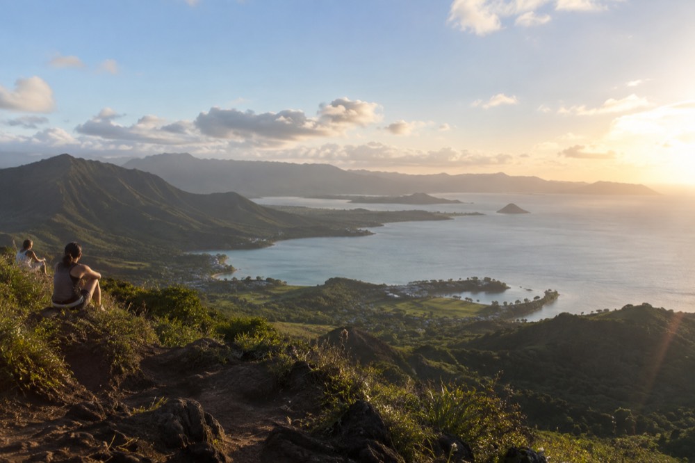 A wide view of Oahu's windward coast with green ridges meeting a calm blue bay