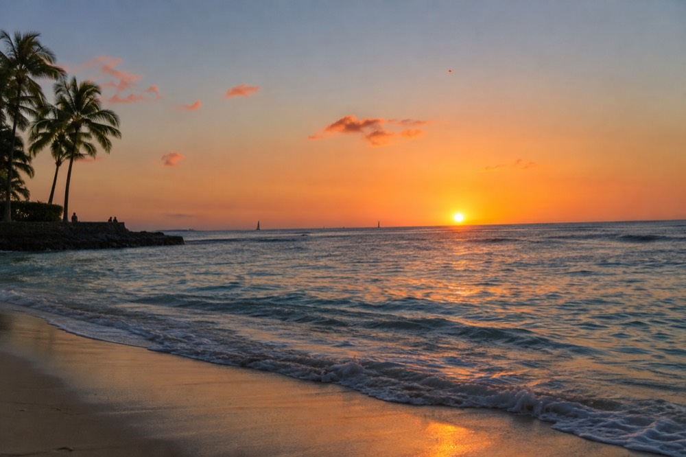 Sun setting over the ocean off a leeward Oahu shoreline with calm water and a clear sky