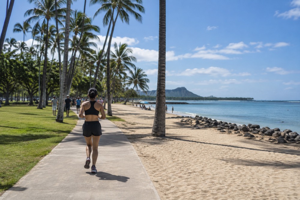 An accessible beach park on Oahu with a paved path running beside the sand, palm trees and calm water beyond