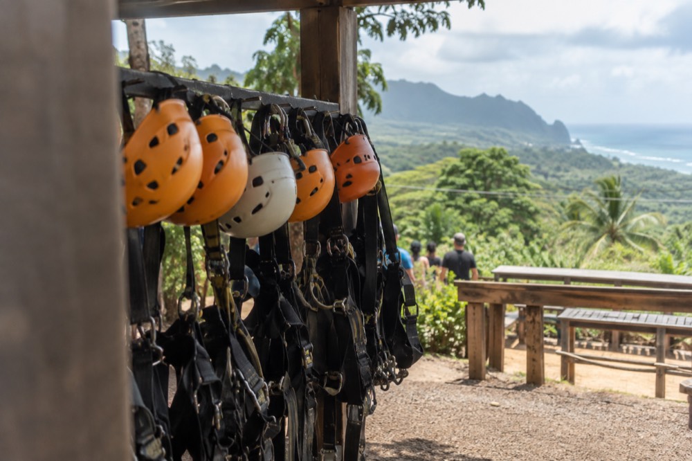 Zipline helmets and harnesses hanging on a rack at a North Shore course check-in area