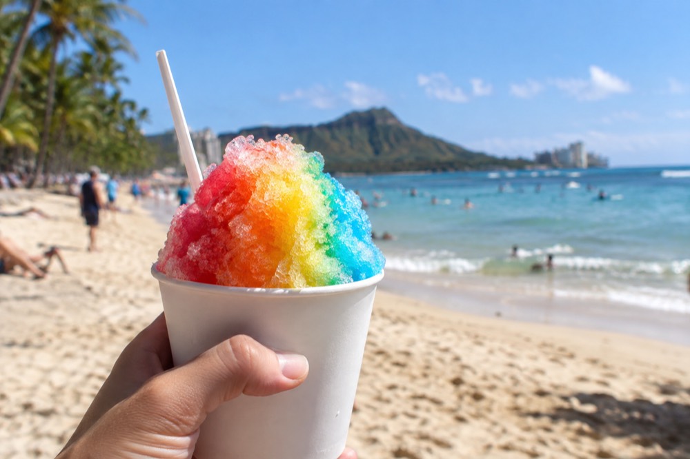 A cup of colorful shave ice held outdoors on a sunny Oahu day