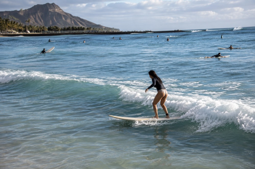 A beginner surfer riding a small whitewater wave on a longboard at Waikiki Beach