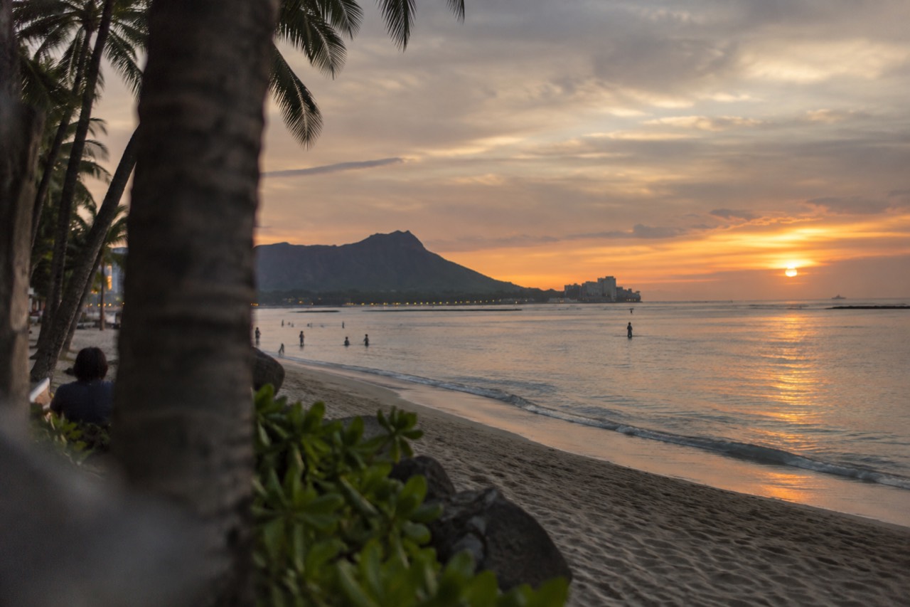 Waikiki beach at dusk with the shoreline lights reflecting on calm water and Diamond Head in the distance