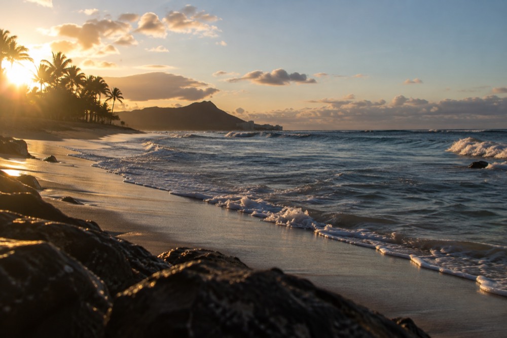 A quiet Oahu beach at golden hour with waves breaking along an empty shoreline