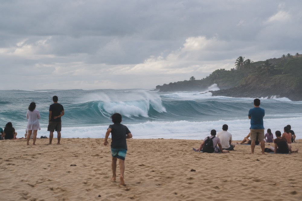 Families watching large waves break at Waimea Bay from a sandy beach