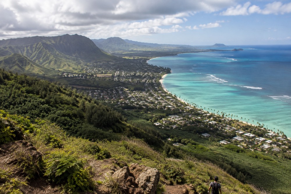 An aerial view of Oahu showing turquoise water along the coast and ridged green mountains inland
