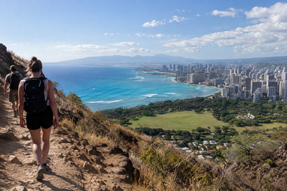 Hikers on a volcanic ridge trail overlooking the Honolulu coastline in morning light