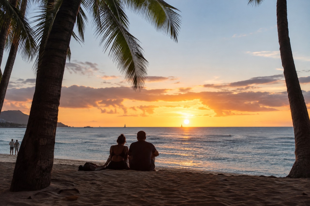 A couple watching the sunset over the ocean from a Waikiki beach with palm trees