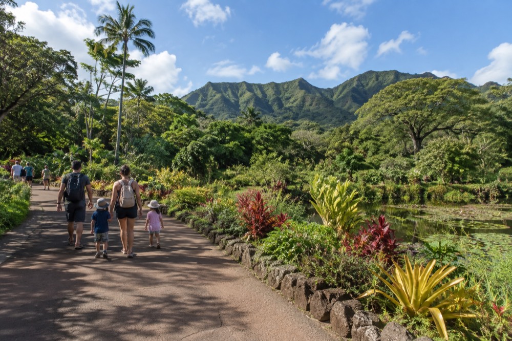 A family walking on a path beside a botanical garden with green mountains in the background