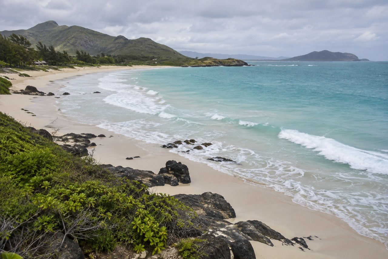 A calm sandy beach in Kailua with gentle waves and green hills behind the shore